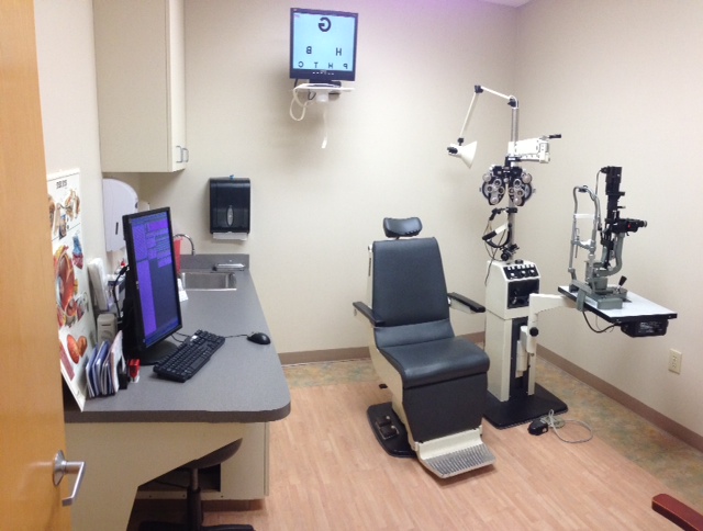 Exam lane with AcuityMaster displaying a chart on the wall-mounted monitor, beside a phoropter and slit lamp